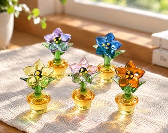 May include: Five miniature glass flower figurines in individual pots. Each features a green stem, a five-petaled blossom in purple, blue, yellow, pink, or orange, and a yellow-centered stamen. The pots are translucent yellow glass.