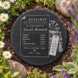 May include: A round black slate memorial plaque featuring an engraved design of a bookshop receipt and a stack of books with a bookmark. The text reads: BOOKSHOP, GOOD BOOKS BRIGHTER SOULS, IN LOVING MEMORY OF Sarah Bennett, 1952-2023, A LIFE WELL LIVED.