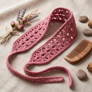 May include: A dusty rose crochet headband featuring a repeating floral motif pattern with openwork details. The headband has long, narrow ties at each end for securing it in place. The construction consists of interconnected circular flower shapes.