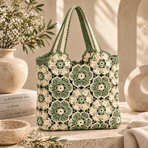 May include: A crochet tote bag constructed from joined floral motifs in alternating shades of sage green and cream. The bag features two integrated handles with a striped pattern and a scalloped top edge, showcasing a detailed yarn texture.