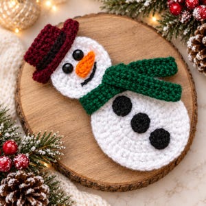 Può includere: Un ornamento a forma di pupazzo di neve all'uncinetto con corpo bianco, cappello rosso scuro con fascia nera, naso a carota arancione brillante, sciarpa verde scuro e tre bottoni circolari neri. Ha due occhi a perla neri e una bocca nera.
