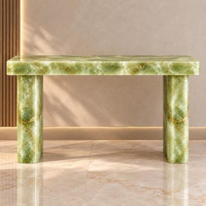 Puede incluir: Una mesa consola rectangular hecha de piedra ónix verde pulida. La pieza presenta una superficie plana y lisa sostenida por dos patas cilíndricas gruesas, mostrando patrones de vetas naturales en tonos esmeralda y verde claro.