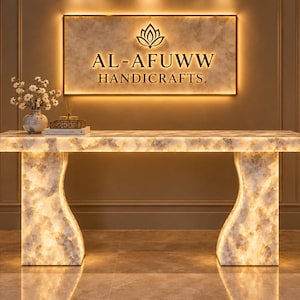 May include: A rectangular console table made of translucent white and grey veined stone with integrated internal lighting. The table features two curved pedestal legs and sits beneath a wall-mounted sign reading AL-AFUWW HANDICRAFTS.
