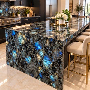 May include: A kitchen island featuring a polished blue and black gemstone countertop with a mosaic-like pattern. The island includes a waterfall edge and is paired with several light-colored upholstered bar stools with gold metal frames.