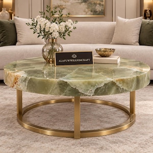 May include: A round coffee table featuring a polished green onyx stone top with natural veining and a gold-colored metal base. A black rectangular sign with the gold text ALAFUWWHANDICRAFT is placed on the surface of the table.