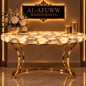 May include: A semi-circular console table featuring a backlit white agate stone top with gold-toned metal legs. The table is positioned below a black sign with gold text reading AL-AFUWW HANDICRAFTS, accompanied by a flower vase and two gold candle holders.