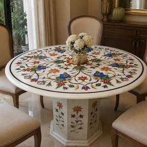 May include: A round white marble dining table featuring intricate floral inlay work with blue, red, yellow, and green stone accents. The table has a central pedestal base with matching floral stone inlay designs and is surrounded by four beige chairs.