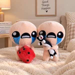 May include: Two plush toys with round peach-colored heads, large black eyes, and blue tear-shaped markings. One plush holds a red six-sided die with black dots, while the other holds a small black and white plush cat with a red collar.