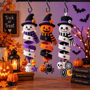 May include: Three hanging crochet Halloween decorations featuring a ghost, a jack-o'-lantern, and a skeleton. Each figure wears a hat and a scarf, with a spiral body adorned with small charms like pumpkins, a cat, a skull, and a coffin.