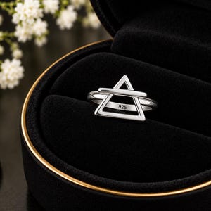May include: A silver ring featuring an open triangular shape with a horizontal bar across the centre. The inner band of the ring is clearly stamped with the number 925, indicating the silver content. The ring is displayed in a black box.