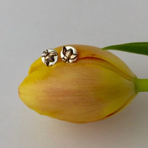 May include: A pair of silver stud earrings with a gold bee design, resting on a yellow tulip.