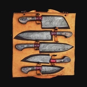 May include: A set of five kitchen knives with Damascus steel blades and wooden handles featuring red accents, each secured in a tan leather roll. The knives vary in blade shape, including a cleaver, chef knives, and paring knives, all displayed.