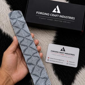 May include: A rectangular metal knife blank featuring a dark gray and silver diamond-patterned finish. Included is a black box labeled Forging Craft Industries Finest Hand Crafted Knives and a white business card with the same company branding.