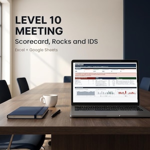 May include: A laptop displaying a Level 10 Meeting dashboard with Scorecard, Rocks, and IDS data in Excel and Google Sheets. A dark blue notebook, a black pen, and a white ceramic mug sit on a wooden conference table in a professional office.