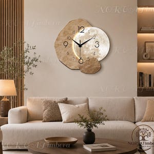 May include: A wall clock featuring an irregular, light-coloured wooden base with a circular, illuminated moon-themed face. The clock has black hour and minute hands, black Arabic numerals, and a warm glow emanating from behind the circular moon element.