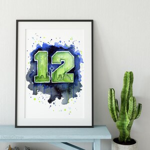 May include: Framed watercolor art print featuring the number "12" in green, with a Seattle skyline silhouette, set against a blue and green watercolor splash background. The artwork is in a black frame.