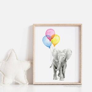 May include: A framed watercolor print featuring a gray elephant holding three colorful balloons. The balloons are pink, blue, and yellow. The artwork is set against a white background and framed in a light wood frame.