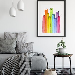 May include: A watercolor painting of a rainbow of cats. The cats are all different colors and have different expressions on their faces. The painting is framed in a black frame and is hanging on a white wall.
