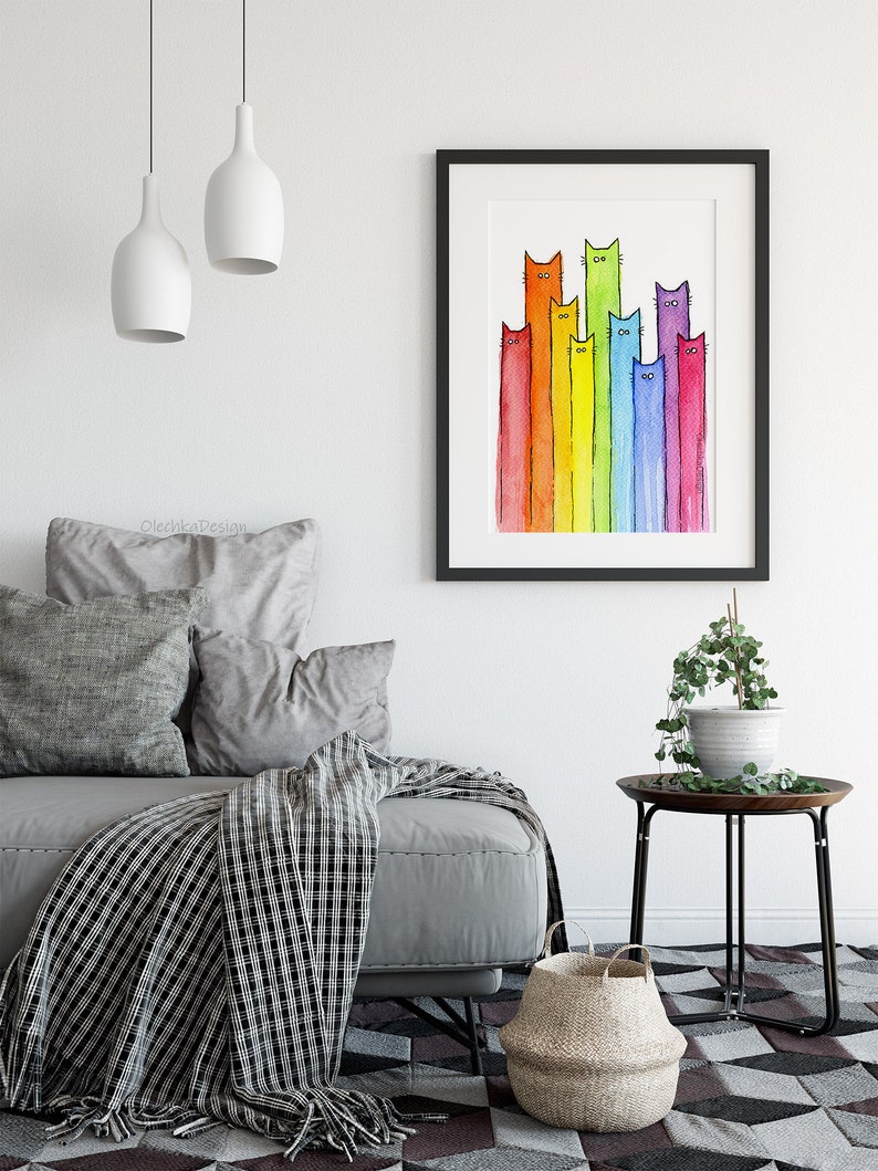 May include: A watercolor painting of a rainbow of cats. The cats are all different colors and have different expressions on their faces. The painting is framed in a black frame and is hanging on a white wall.