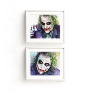 May include: Two framed watercolor paintings of the Joker from the movie The Dark Knight. The Joker is depicted with a green and purple background and a sinister smile. The top painting shows the Joker holding a playing card. The bottom painting shows the Joker looking directly at the viewer.