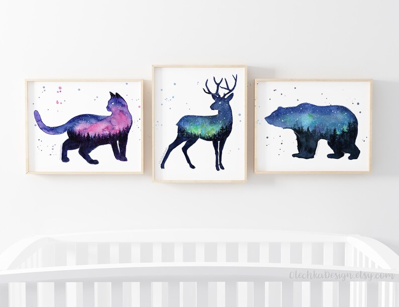 May include: Three watercolor prints featuring silhouettes of a cat, deer, and bear with a starry night sky and forest scene inside each animal. The prints are framed in natural wood.