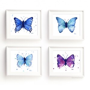 May include: Set of four watercolor paintings of butterflies in shades of blue and purple. Each butterfly is surrounded by small white dots on a white background. The paintings are framed in white frames.