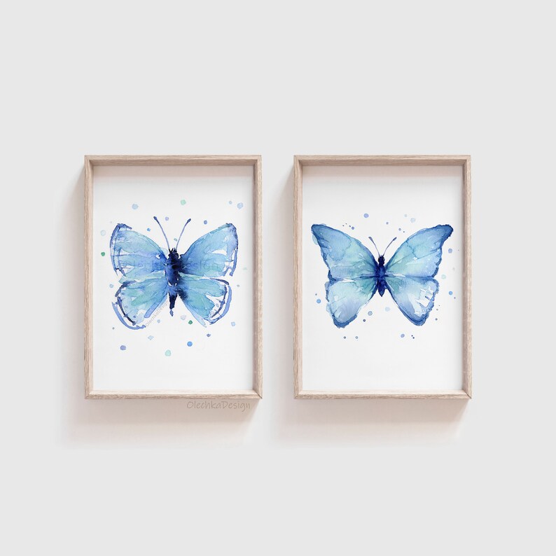 May include: Two framed watercolor paintings of blue butterflies on a white background. Each butterfly is surrounded by small blue and green dots.