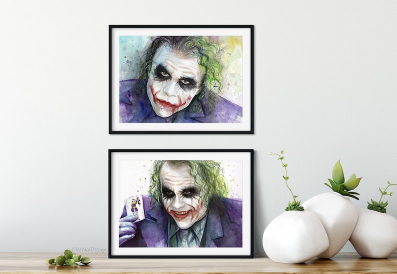 May include: Two framed watercolor paintings of the Joker from the movie The Dark Knight. The top painting shows the Joker's face with a sinister smile. The bottom painting shows the Joker holding a playing card with the Joker's face on it.