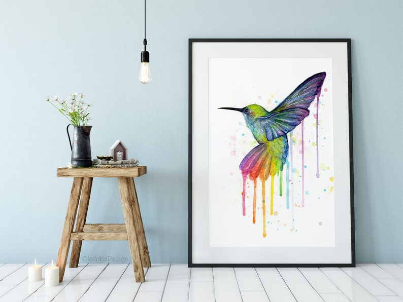 May include: A watercolor painting of a colorful hummingbird with rainbow-colored drips. The hummingbird is flying with its wings spread out. The background is white with a few watercolor splatters.