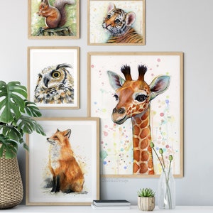 Peut inclure: Un ensemble de cinq peintures &agrave; l'aquarelle encadr&eacute;es repr&eacute;sentant diff&eacute;rents animaux. Les peintures comprennent un &eacute;cureuil, un ourson tigre, un hibou, une girafe et un renard. Les peintures sont toutes dans un cadre en bois clair et sont dispos&eacute;es sur un mur blanc.
