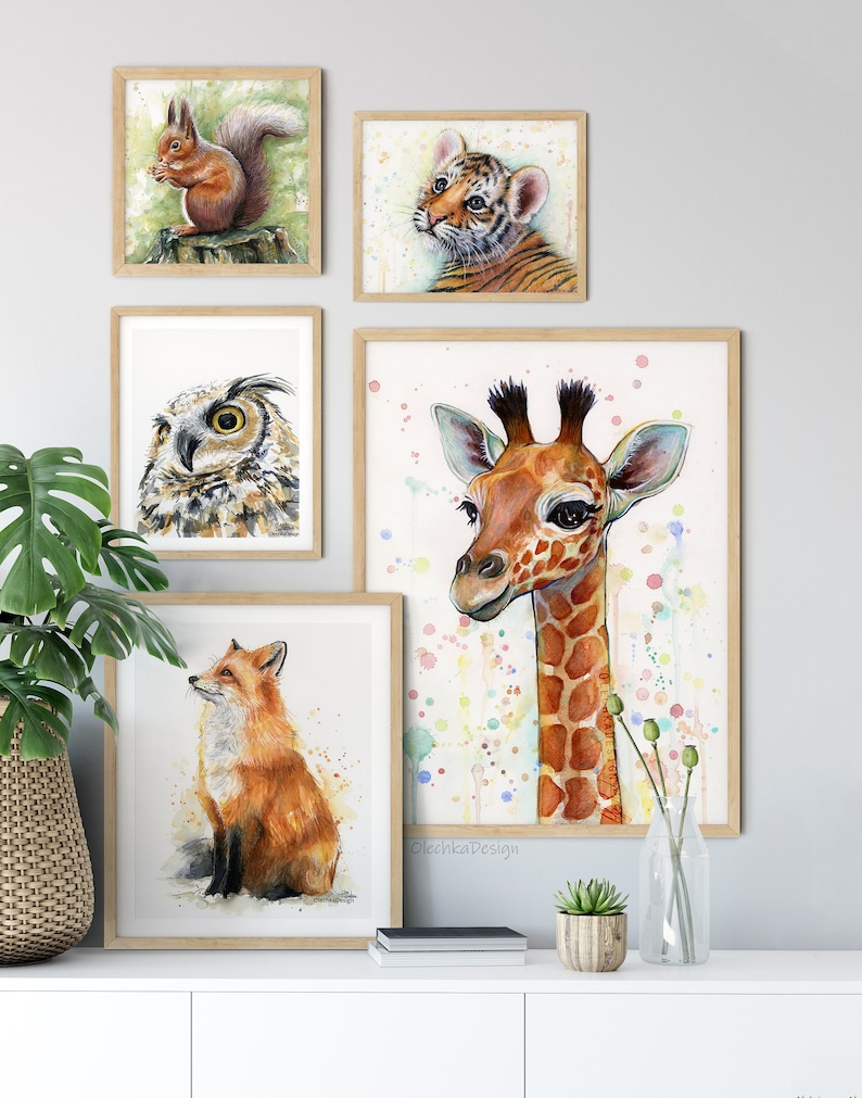 May include: A set of five framed watercolour paintings featuring various animals. The paintings include a squirrel, a tiger cub, an owl, a giraffe, and a fox. The paintings are all in a light wood frame and are arranged on a white wall.