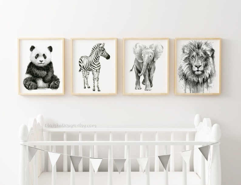 May include: Four framed animal art prints in black and white. The prints feature a panda, zebra, elephant, and lion. The frames are light wood, and the artwork is displayed above a white crib with a gray and white pennant banner.