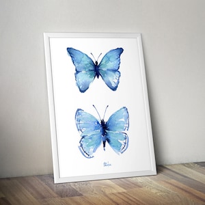 May include: A framed watercolor painting of two blue butterflies. The butterflies are painted in a realistic style with delicate details. The painting is on a white background.