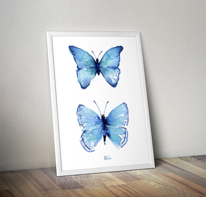 May include: A framed watercolor painting of two blue butterflies. The butterflies are painted in a realistic style with delicate details. The painting is on a white background.