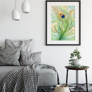 May include: A watercolor painting of a peacock feather with a blue eye, surrounded by green and yellow swirls and water droplets. The painting is framed in black and hanging on a white wall above a gray couch.