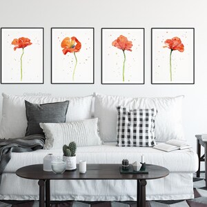 May include: Four framed watercolor paintings of red poppies on a white background. The paintings are hanging on a white wall above a white couch with pillows and a throw blanket.