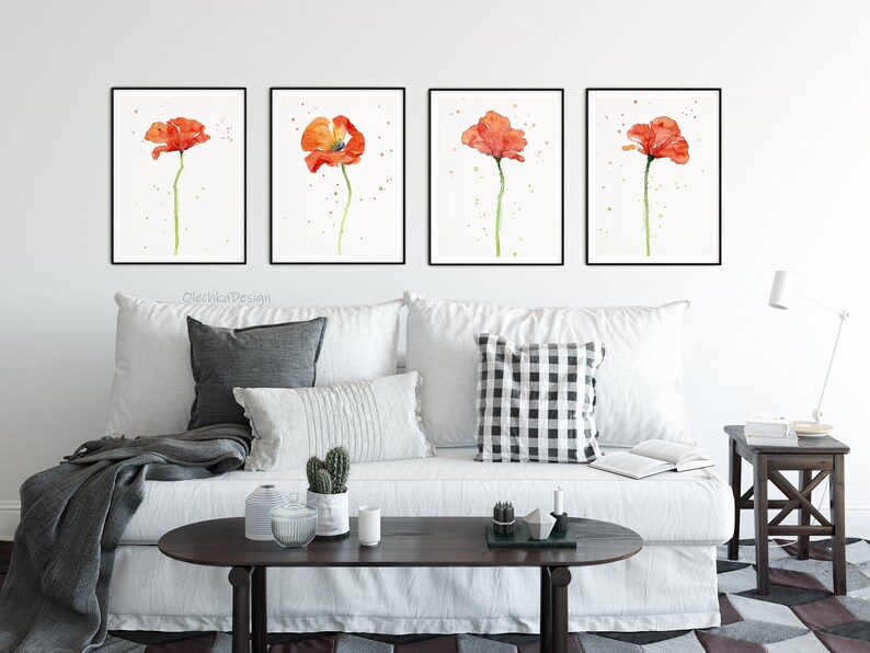 May include: Four framed watercolor paintings of red poppies on a white background. The paintings are hanging on a white wall above a white couch with pillows and a throw blanket.