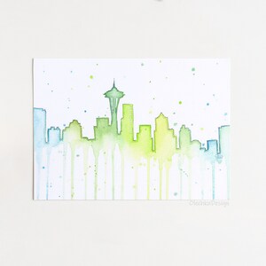 May include: Watercolor painting of the Seattle skyline with the Space Needle in the center. The buildings are outlined in green and blue, with watercolor drips running down the page. The background is white with light blue and green watercolor splatters.