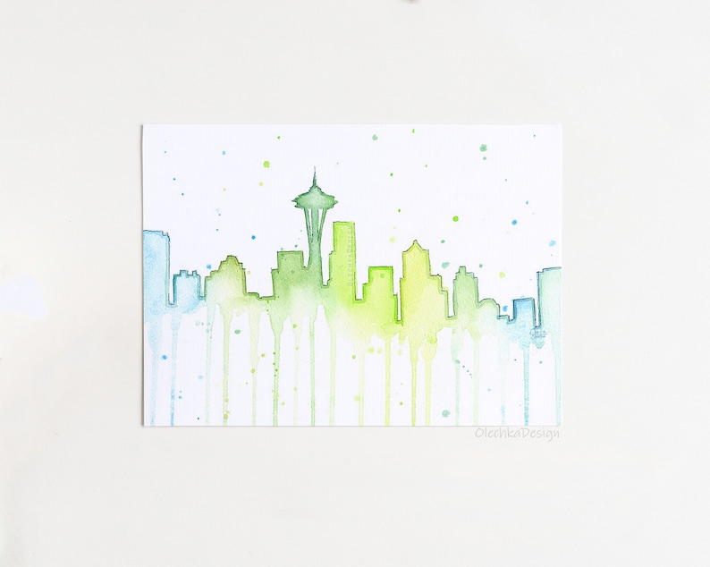 May include: Watercolor painting of the Seattle skyline with the Space Needle in the center. The buildings are outlined in green and blue, with watercolor drips running down the page. The background is white with light blue and green watercolor splatters.