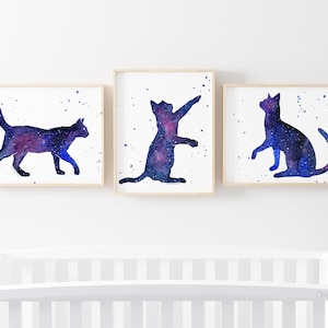 May include: Three watercolor paintings of galaxy cats. Each cat is a different pose, with a blue and purple galaxy pattern.