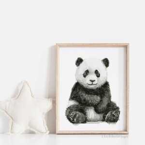 May include: A framed watercolor print of a panda bear sitting. The panda is black and white with a soft, textured appearance. The frame is light-colored wood. A white star-shaped pillow is to the left of the frame.