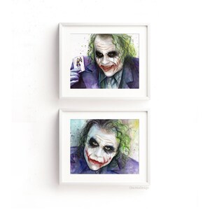 May include: Two framed watercolour paintings of the Joker from the film The Dark Knight. The Joker is depicted with a green and purple colour scheme, a sinister smile, and a green and purple suit. The top painting shows the Joker holding a playing card. The bottom painting shows the Joker's face close up.