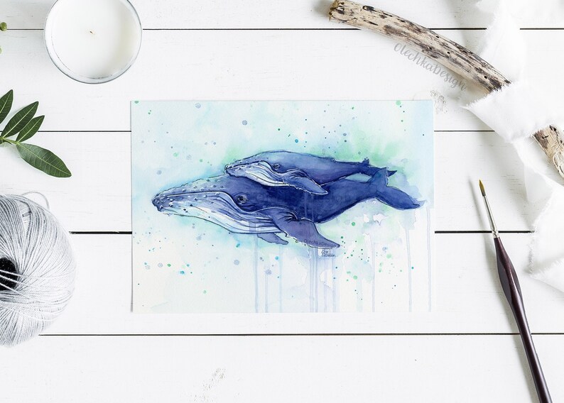 May include: Watercolor painting of two blue whales swimming together. The larger whale is in the foreground and the smaller whale is swimming on top of it. The painting has a light blue background with green and blue watercolor splatters.
