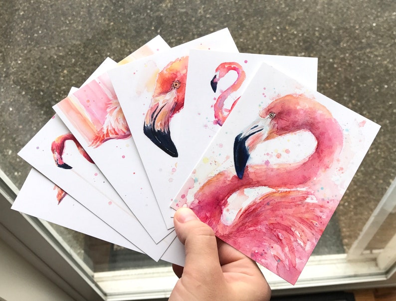 May include: Five watercolor paintings of pink flamingos on white card stock. The paintings are in various poses, including a flamingo with its head turned to the side, a flamingo with its neck curved, and a flamingo with its wings spread.