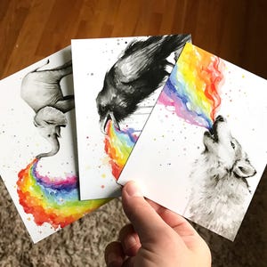 May include: Three watercolor paintings on white cardstock. Each painting features a different animal: an elephant, a raven, and a wolf. Each animal is blowing a rainbow out of its mouth.