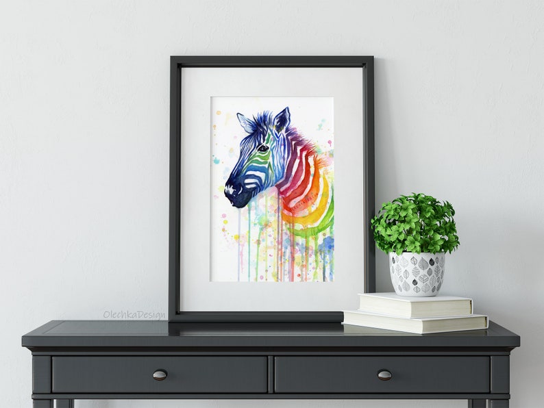 May include: A watercolor painting of a zebra with a rainbow pattern on its stripes. The zebra is facing to the left and has a white background. The painting is framed in a black frame.