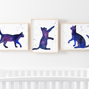 Pode incluir: Tr&ecirc;s pinturas de aquarela de gatos gal&aacute;xia. Cada gato est&aacute; em uma pose diferente, com um padr&atilde;o de gal&aacute;xia azul e roxo.