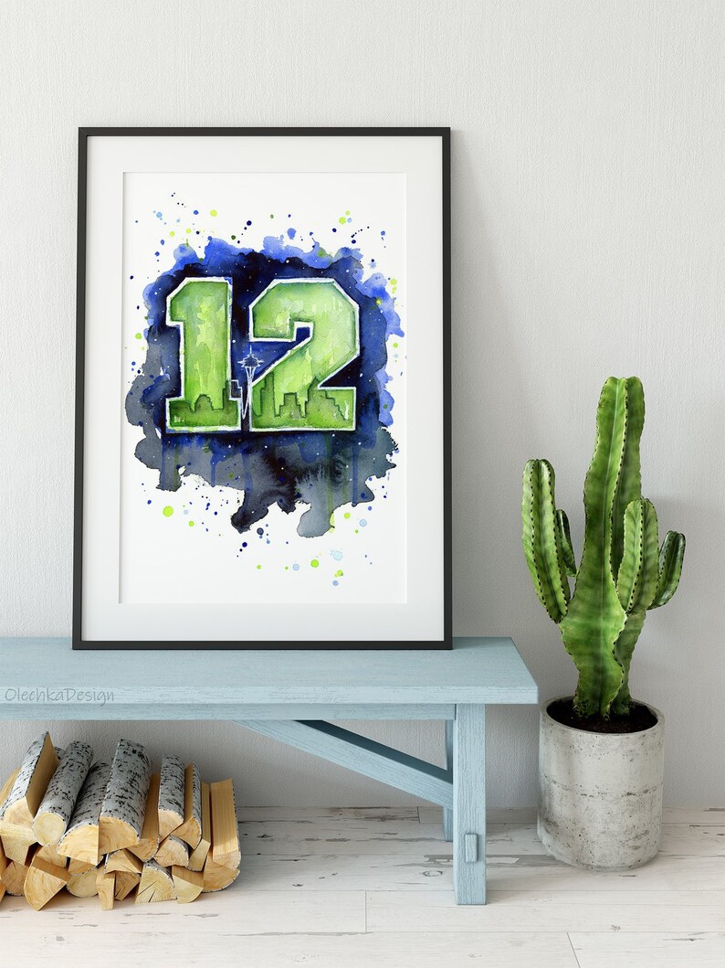 May include: Framed watercolor art print featuring the number "12" in green, with a Seattle skyline silhouette, set against a blue and green watercolor splash background. The artwork is in a black frame.