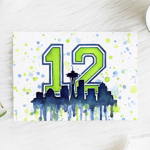 May include: Watercolor painting of the number 12 in green and blue with a silhouette of the Seattle skyline, including the Space Needle, in the center. The background is white with green and blue watercolor splatters.
