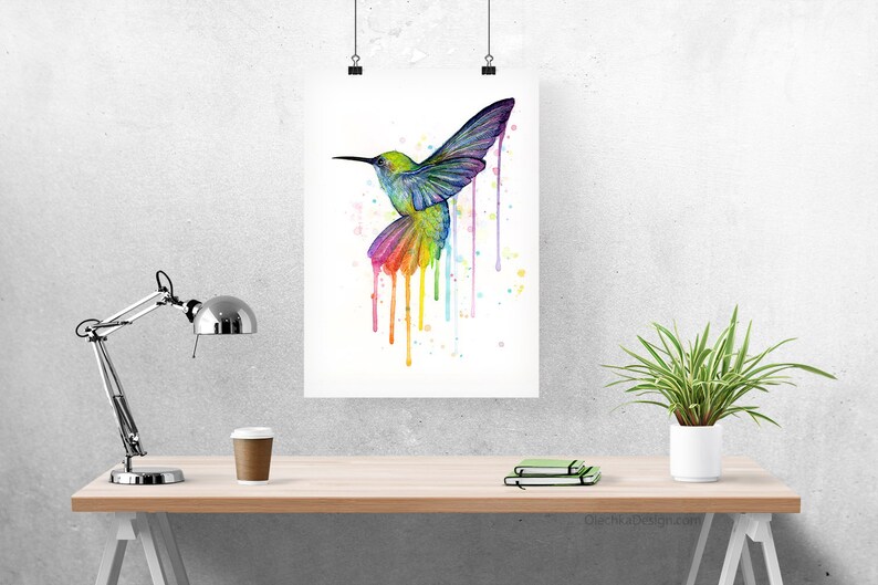 May include: A watercolor painting of a hummingbird in flight with a rainbow of colors dripping from its wings. The background is white with a few scattered paint splatters.